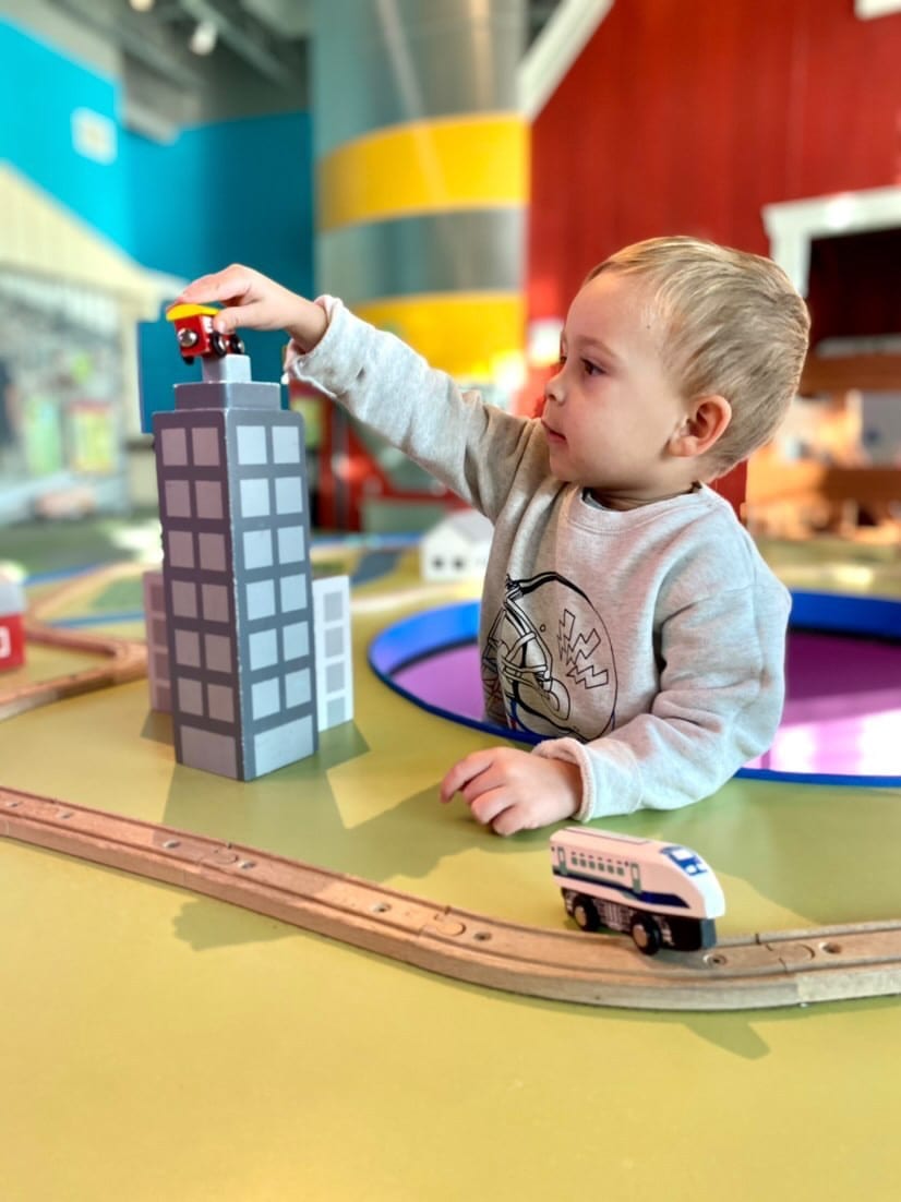 Child playing with train table in toddler exhibit.