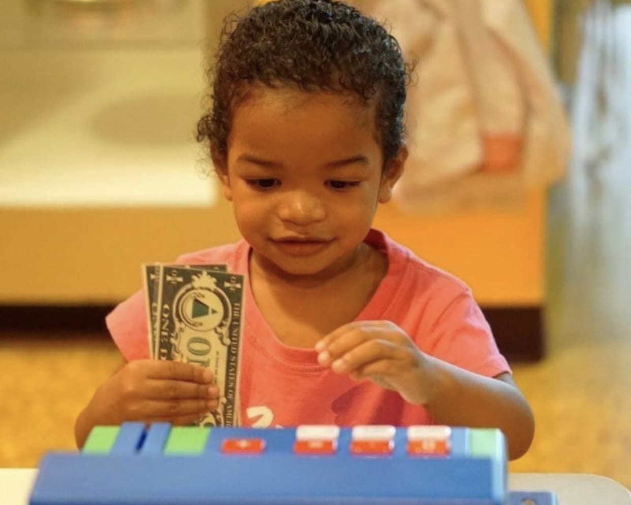 Kid putting play money into cash register in exhibit.